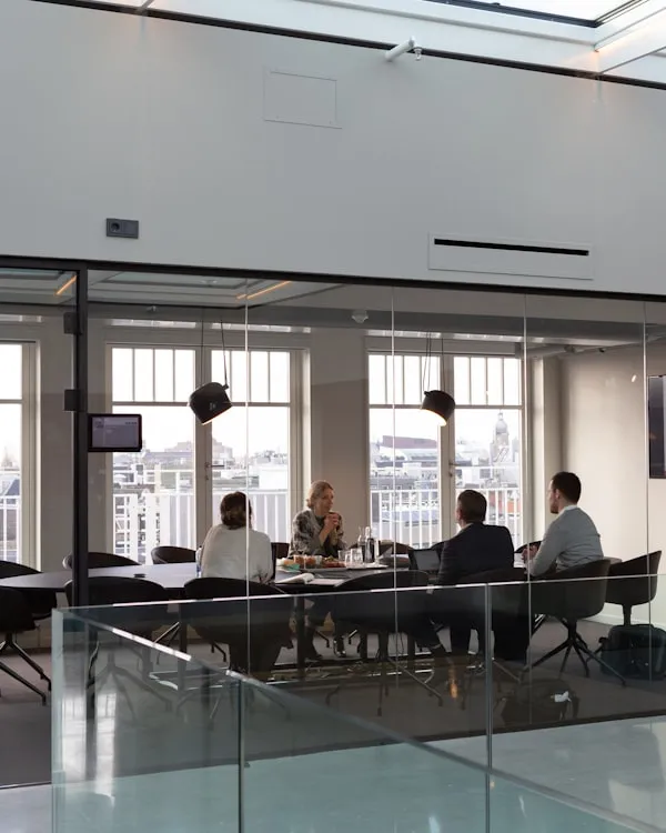 A modern high-rise board room with a large wooden table and chairs, representing corporate partners.